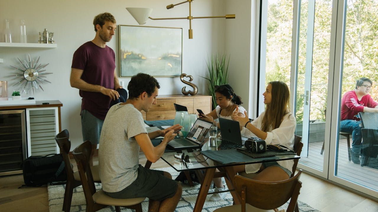 Group of young adults collaborating indoors with laptops and devices.